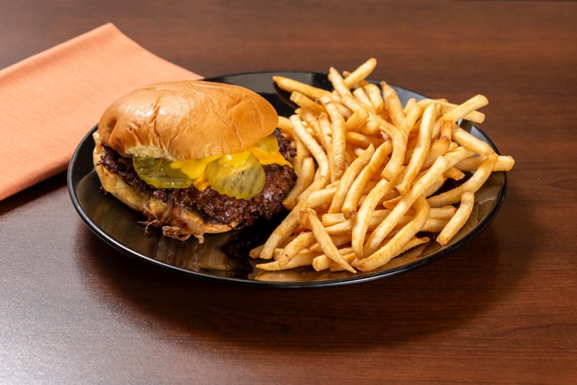 Cheeseburger with pickles and caramelized onions, served with a side of golden french fries.