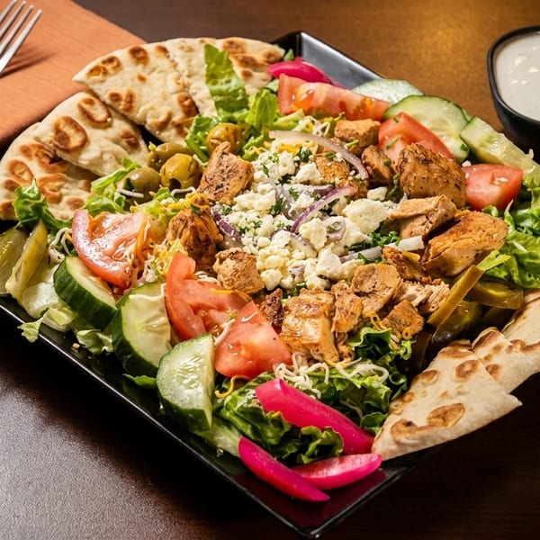 Chicken shawarma salad with pita bread, tomatoes, cucumbers, olives, and feta cheese.